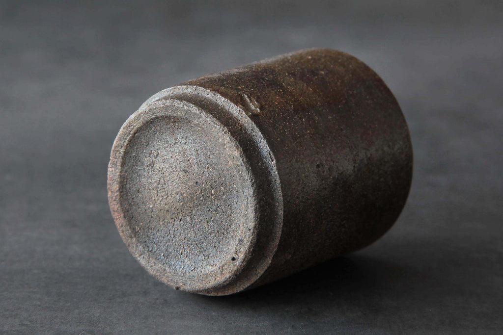 Bizen ware tea cup shown on its side, highlighting the rough clay base and natural earthy brown surface texture.