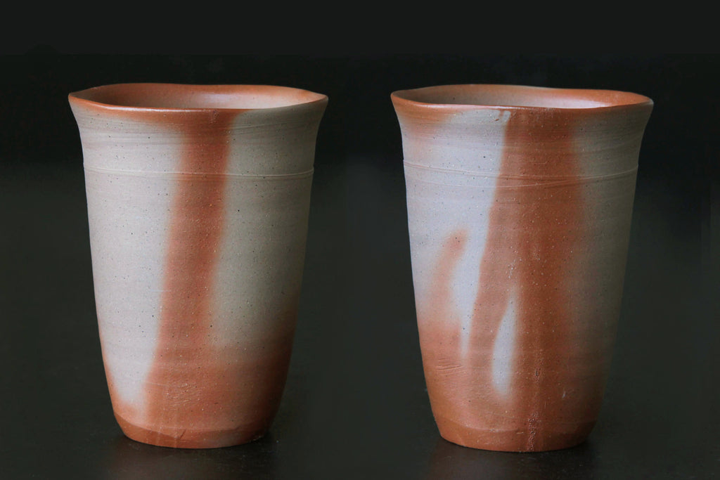 Pair of Bizen ware beer tumblers with reddish flame-like effects on dark background