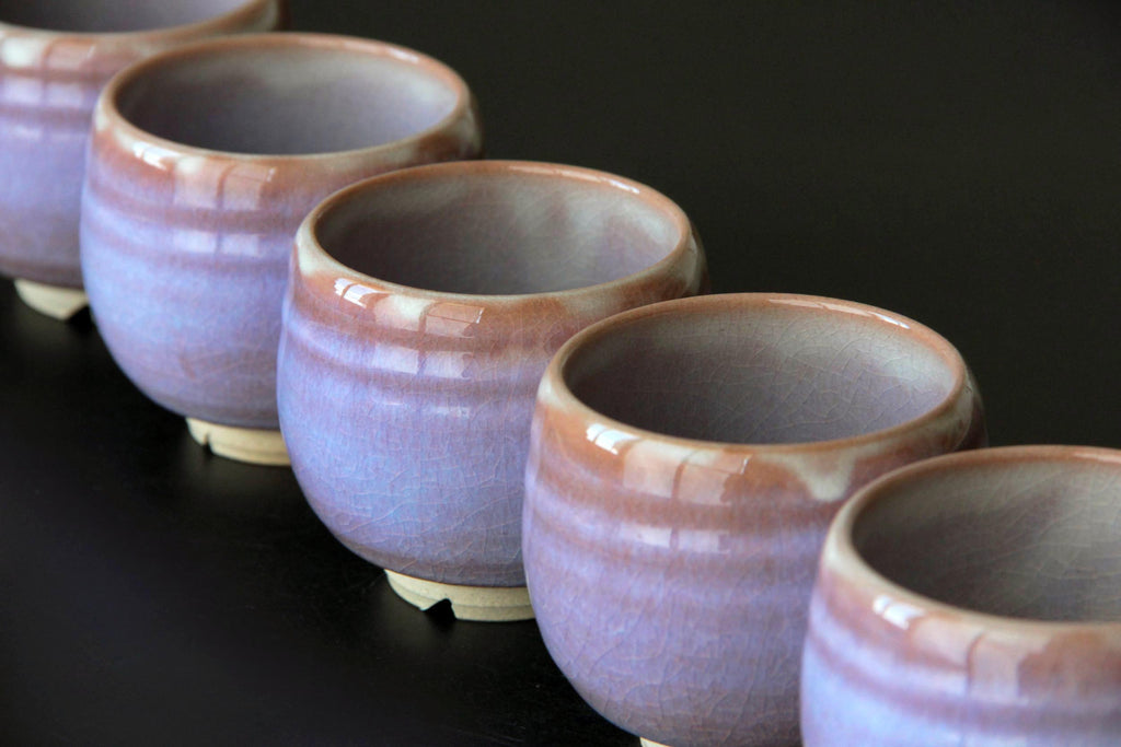 Row of handcrafted Hagi ware yunomi cups with soft pink and purple glaze, displayed in
diagonal formation