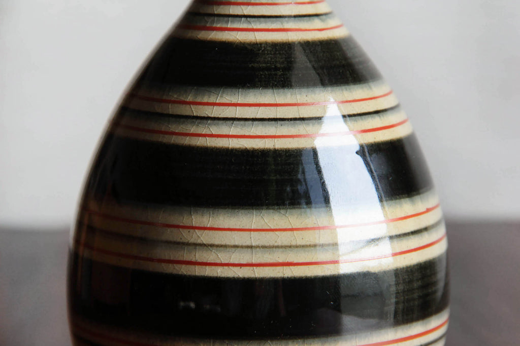 Close-up of striped Hasami-yaki sake bottle showing glossy surface with red and black lines.