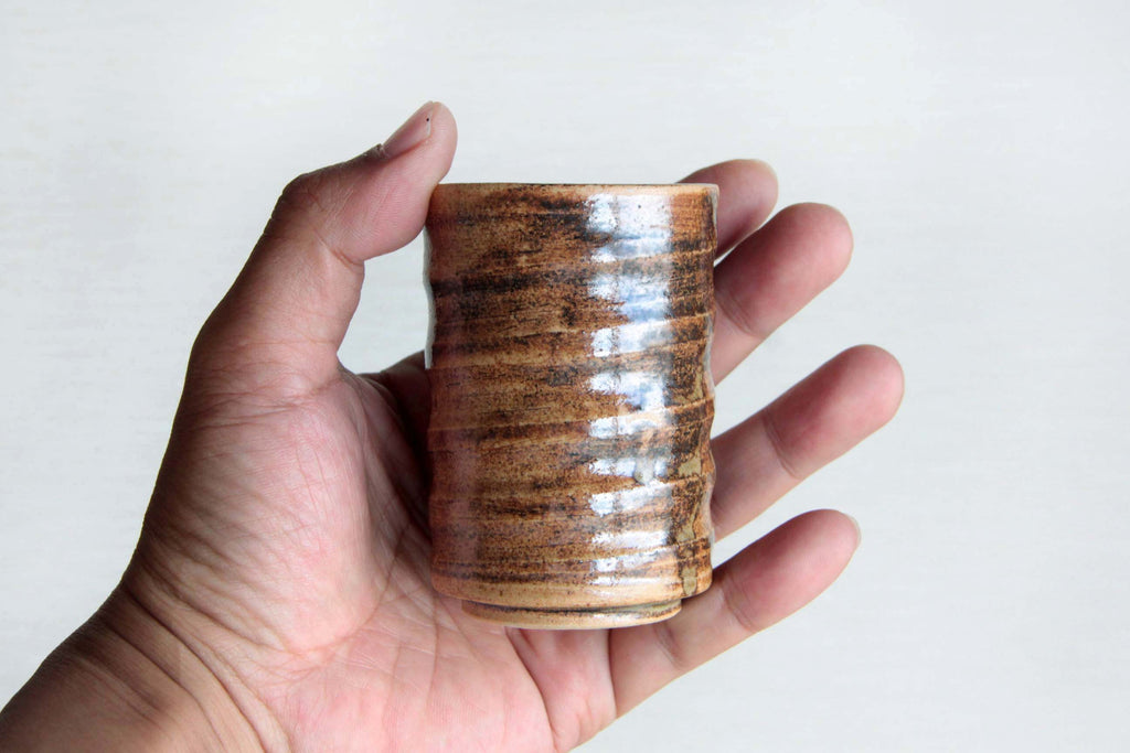 Brown ceramic tea cups. Showing the size by holding 