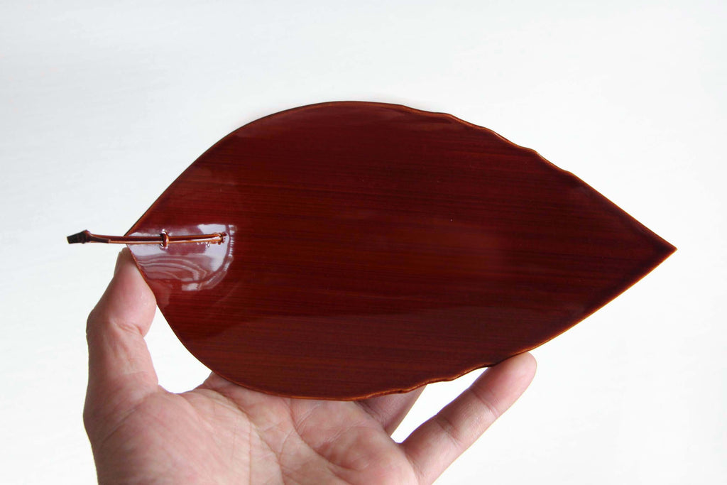 Hand holding a lacquered leaf-shaped plate, showing size and lightweight design
