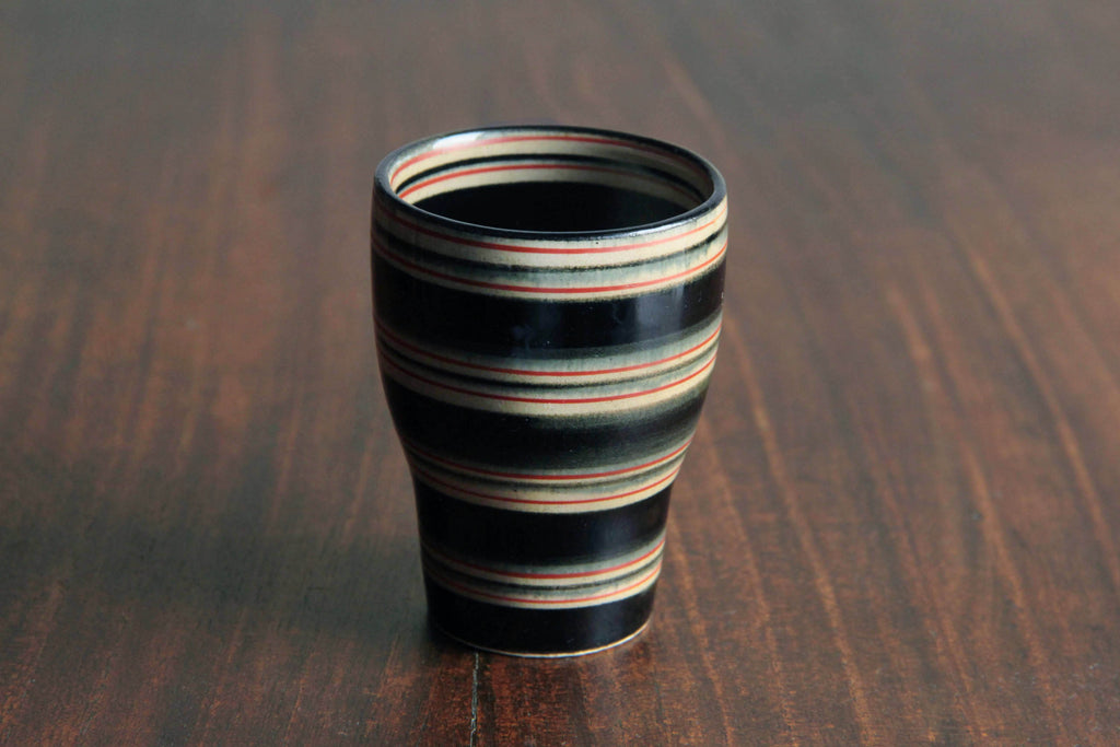 Angled front view of a striped Hasami
yunomi on wood with soft lighting
showing color variation in glaze