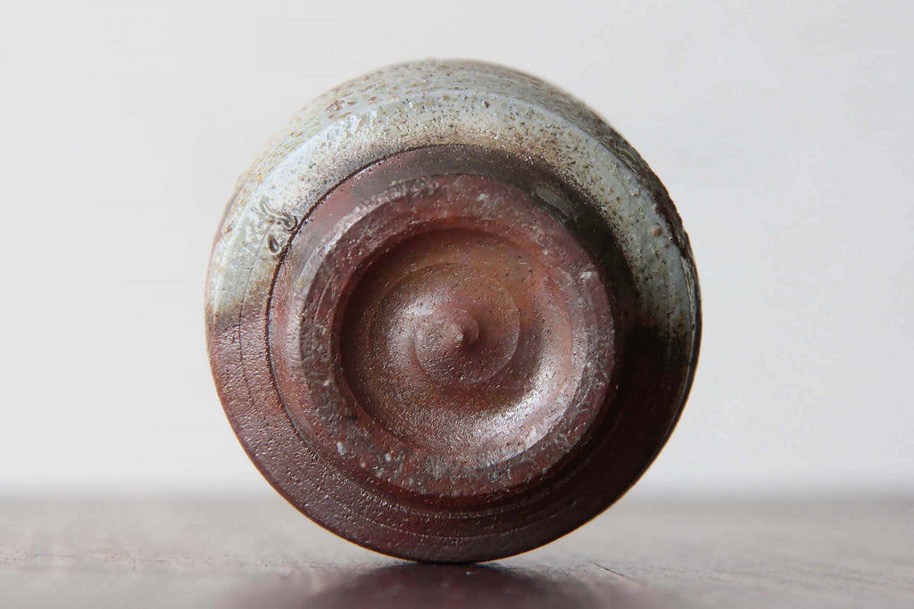 Close-up of the base of a Bizen ware sake cup, showing the circular foot ring and natural reddish-brown and gray firing patterns.