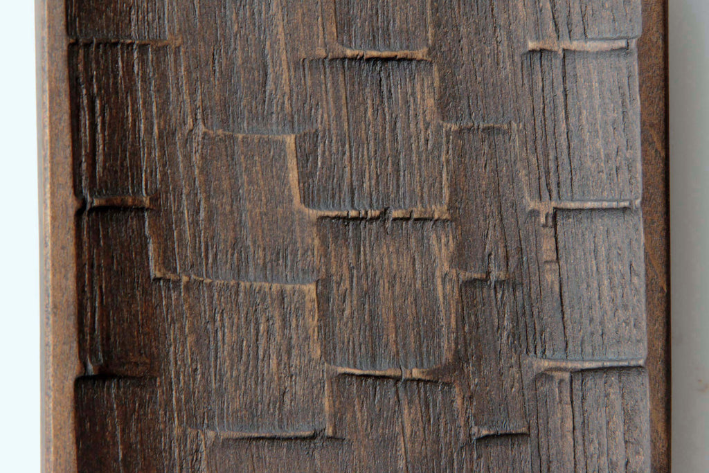 Close-up of Japanese hand-carved wooden plate showing detailed chisel marks in a geometric pattern.