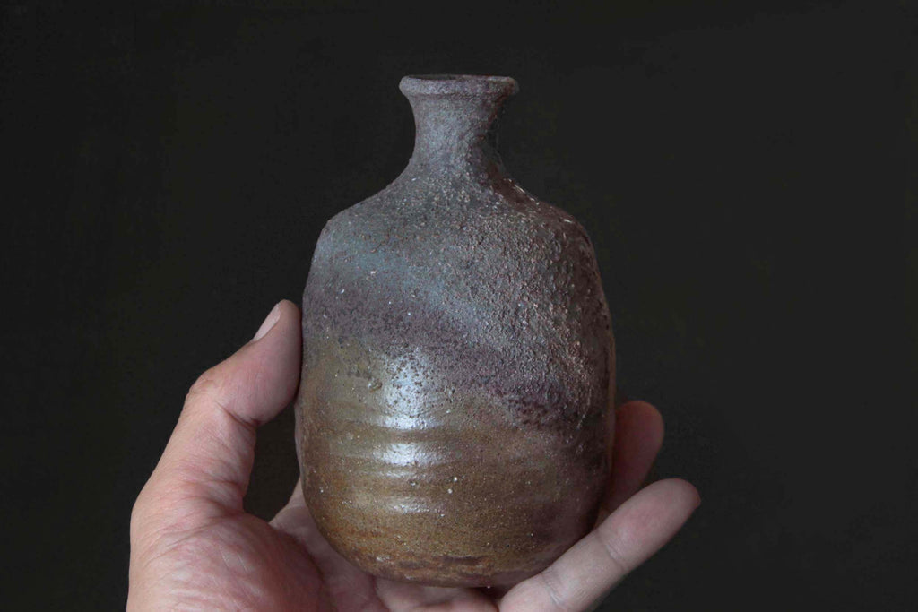 Bizen sake bottle held in hand, demonstrating size, shape,
and coarse unglazed texture with gradation of firing marks.