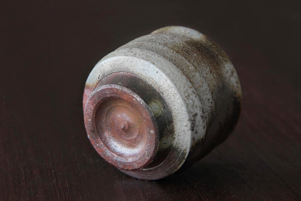 Bizen ware sake cup shown on its side, highlighting the circular foot and multicolored natural firing patterns in red, brown, and white.