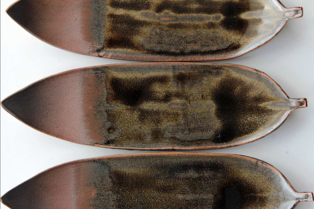 Three Echizen-yaki bamboo leaf plates stacked horizontally, showing glaze gradation from dark
brown to reddish tones.