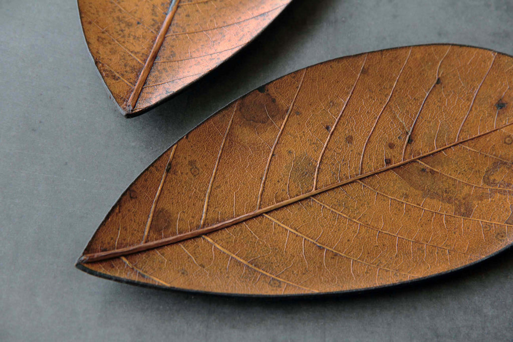 Close-up of handcrafted Japanese plate made from a real leaf, showing natural veins and organic patterns in brown tones.