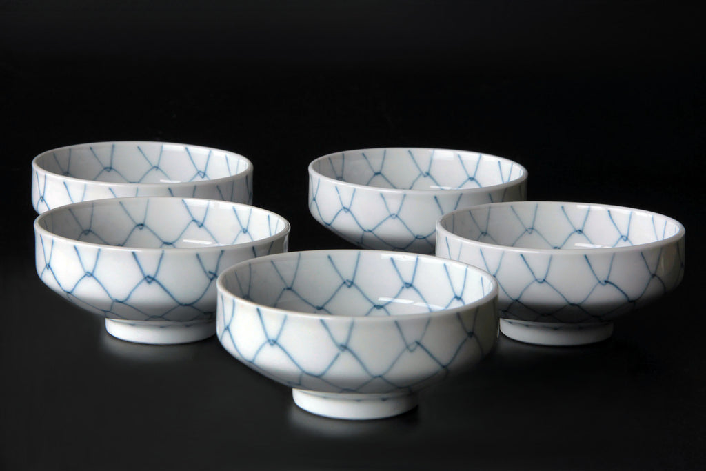 Five Japanese porcelain bowls standing upright showing blue net pattern on white background