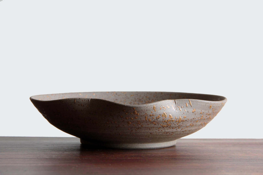 Side view of handcrafted Japanese tableware with curved lip and warm gray glaze,
