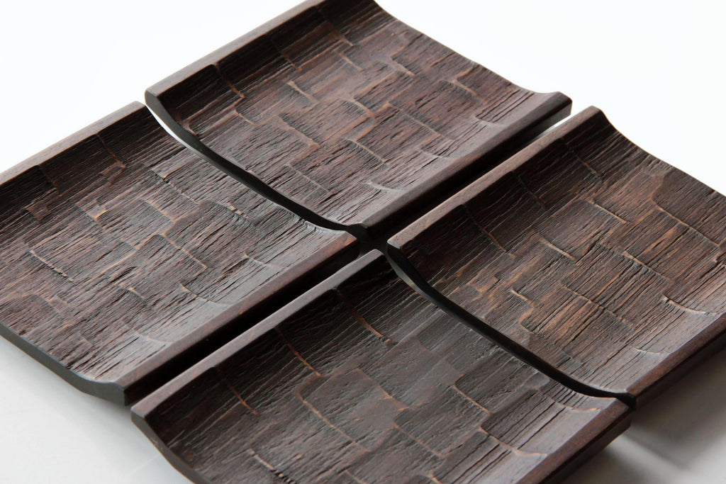 Set of four Japanese square wooden plates with textured carved surfaces, arranged together on a white background.