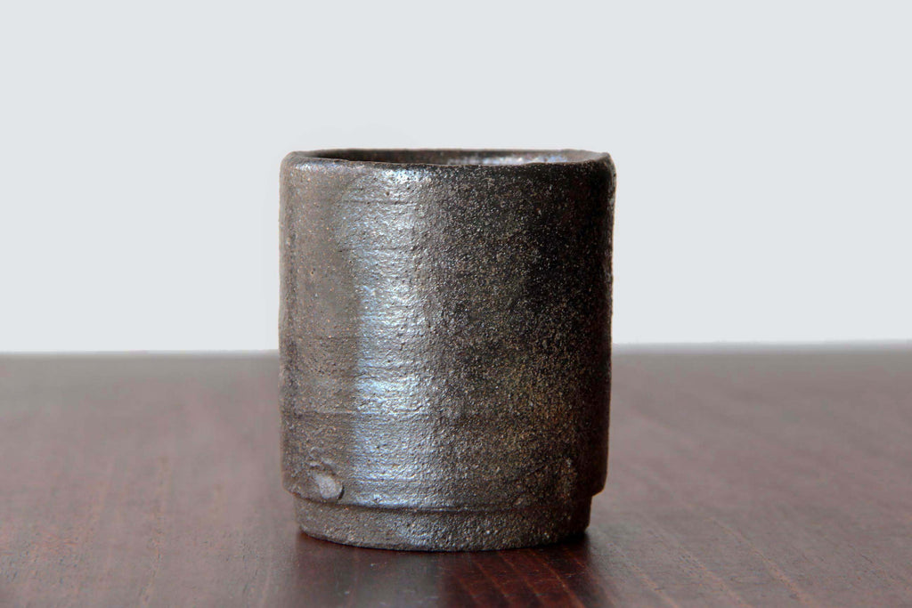 Bizen ware tea cup with dark earthy tones and natural textured surface, placed on a wooden table.