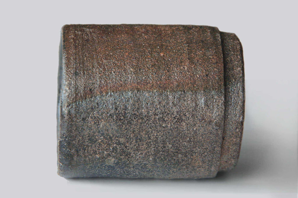 Bizen ware tea cup placed on its side, highlighting the rough unglazed clay texture with natural earthy brown and gray firing patterns.
