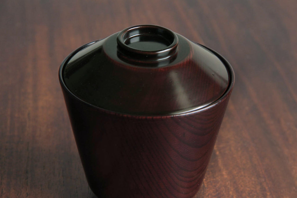 Close-up of a Japanese lacquered bowl with visible wood grain, placed on a wooden surface.