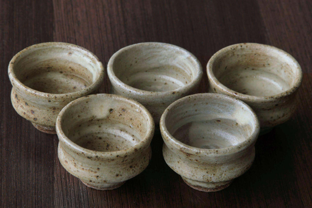 Group of five Mashiko pottery sake cups, arranged together
on wooden surface.