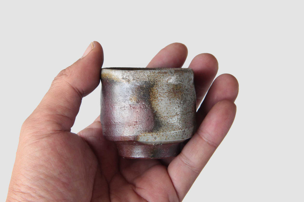 Hand-held view of Bizen ware sake cup, highlighting its small size and textured unglazed surface with multicolored natural kiln effects.