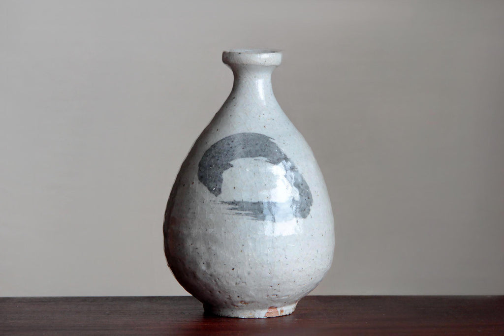 Big size Sake bottle with white glaze. Standing on the brown table