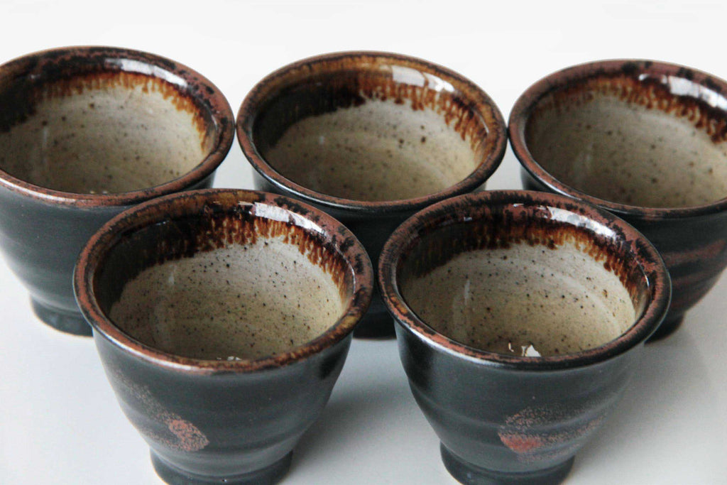 Five Satsuma yunomi tea cups with dark glaze exterior and speckled interior displayed in
formation