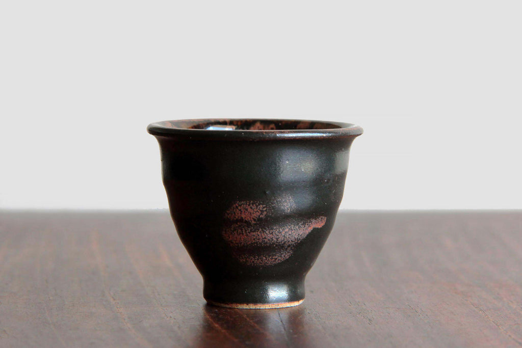 Side view of a Satsuma ware yunomi cup with glossy black glaze and reddish firing accents