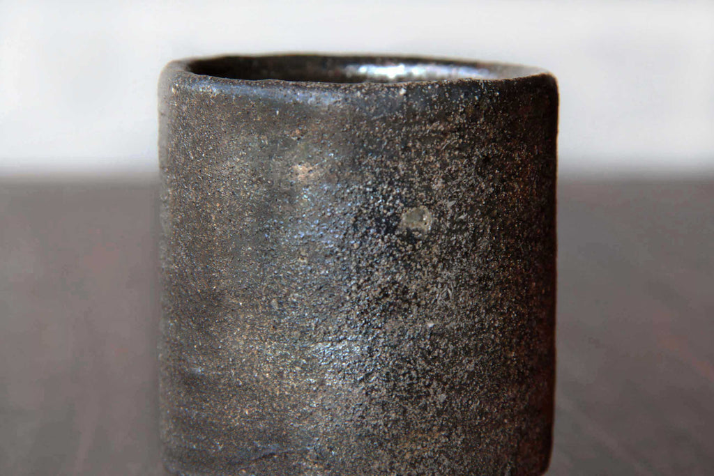 Close-up of a Bizen ware tea cup, showing the unglazed rough-textured clay surface with natural earthy dark brown tones.
