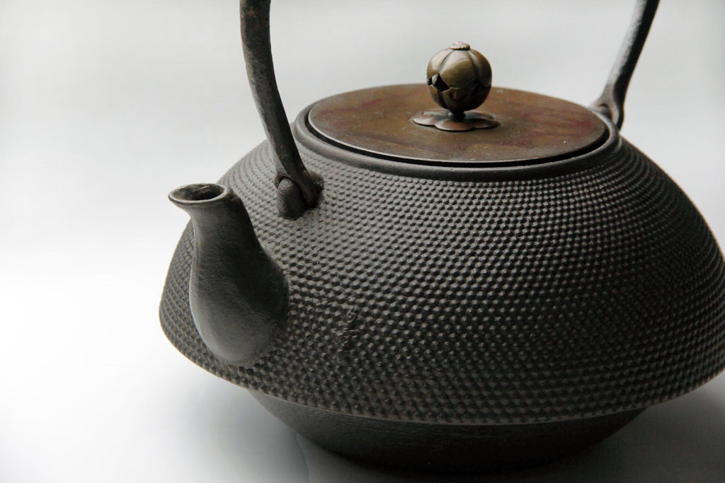 Vintage Japanese cast iron kettle (Tetsubin) with hobnail texture, bronze lid, and ornate spherical knob on a light background