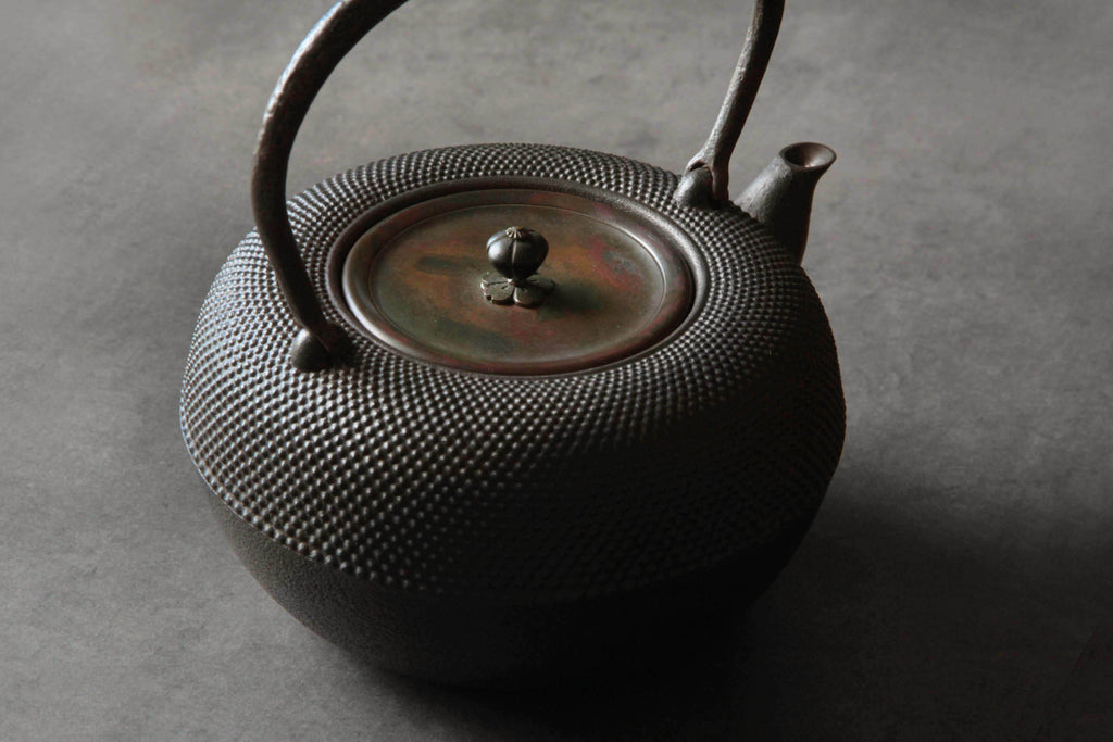 Japanese cast iron kettle with copper lid photographed on a dark surface