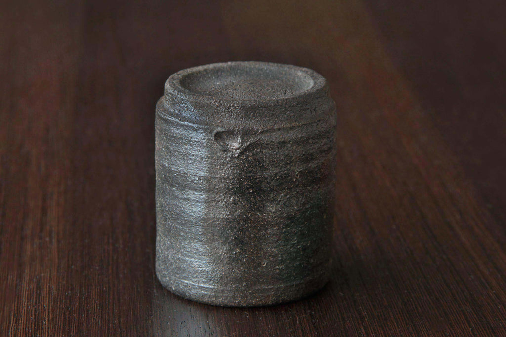 Bizen ware tea cup placed upside down on a wooden surface, showing the unglazed clay foot and natural earthy dark brown texture.
