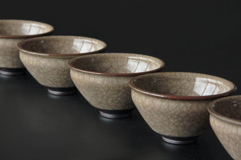 Row of Japanese yunomi tea bowls with refined crackle glaze and reddish rim accent