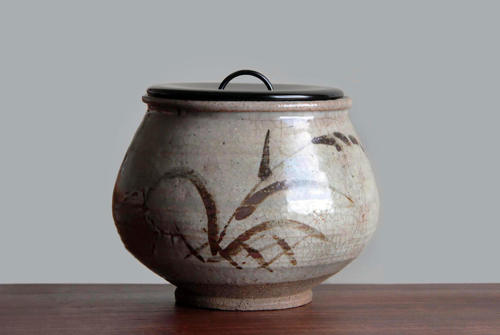 Front view of an antique Karatsu ware mizusashi with a black lacquered lid.
