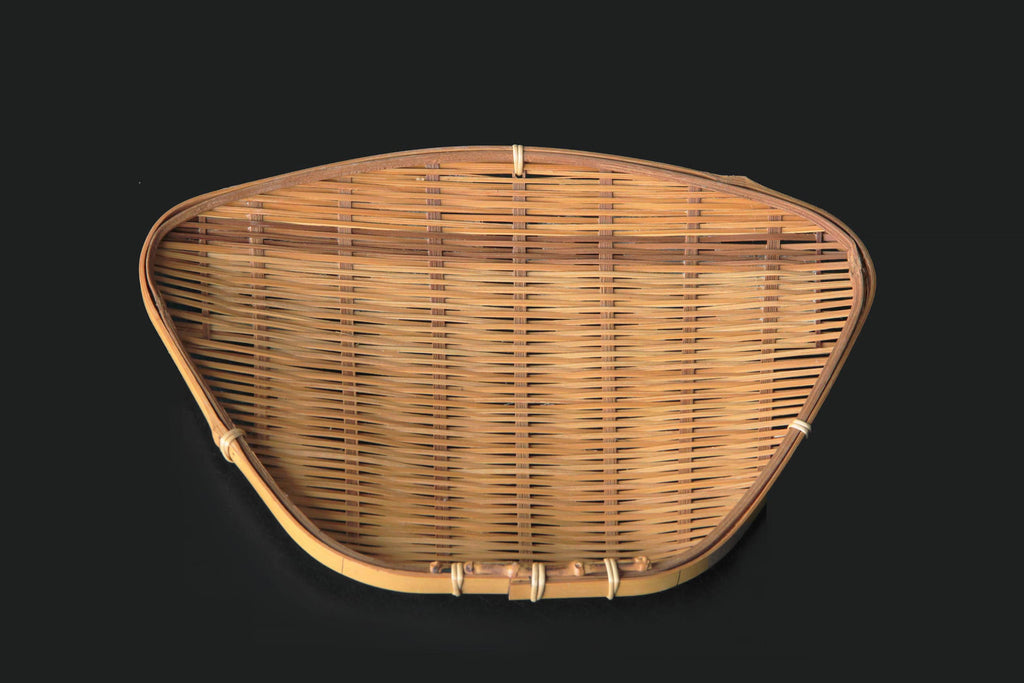 Triangular hand-woven bamboo tray with warm natural color on a black background
