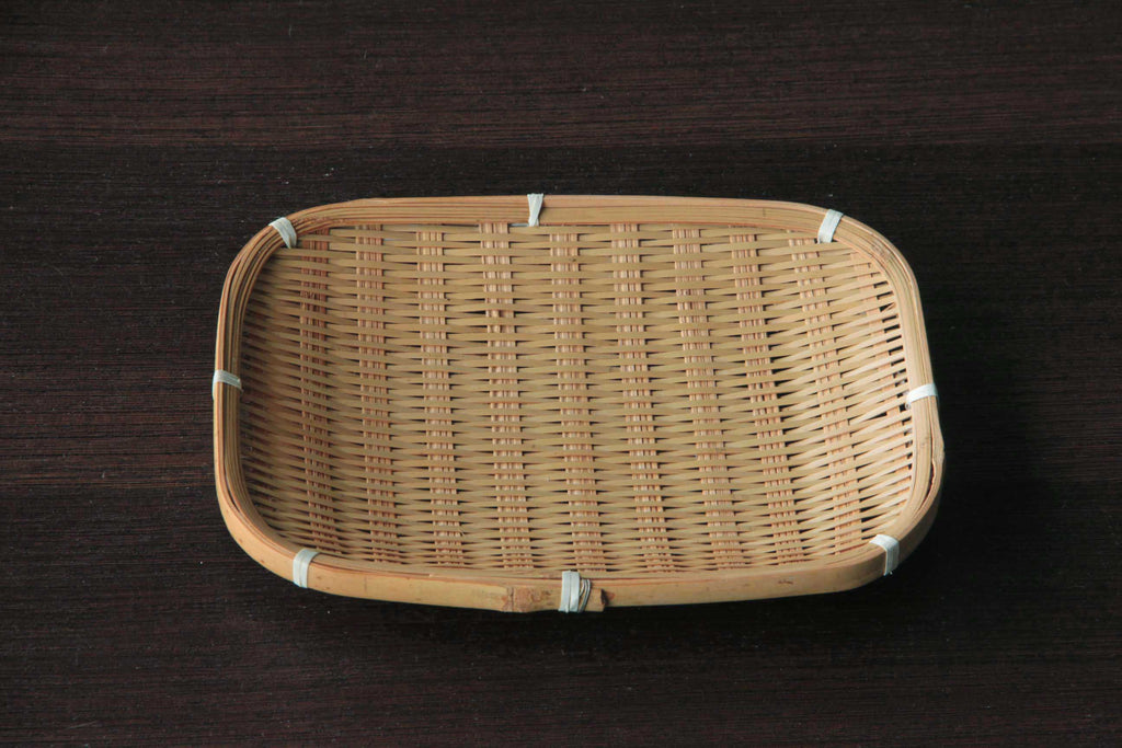 Rectangular hand-woven bamboo tray with white bindings displayed on a dark wooden surface