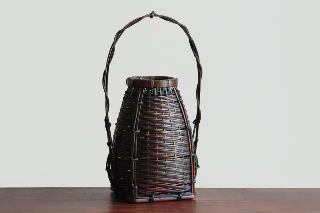 Dark brown Japanese bamboo flower basket vase with twisted natural handle and tapered woven body