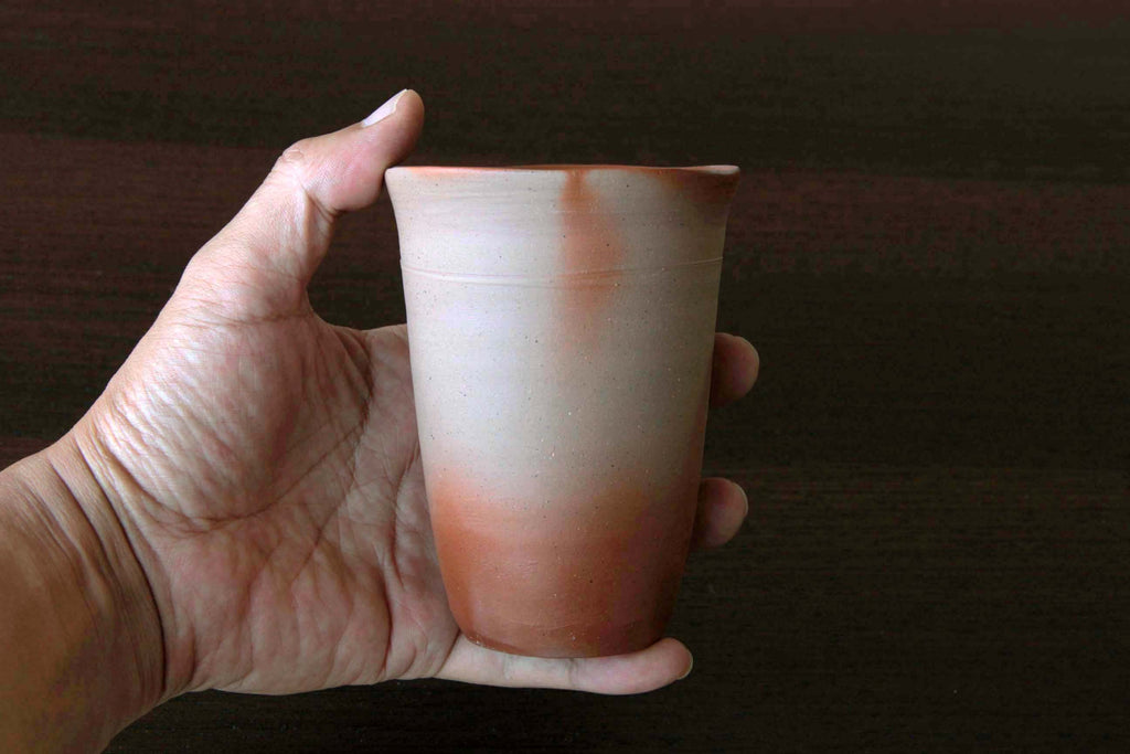 Hand holding a Bizen ware beer cup with a natural flame-kissed pattern and smooth form