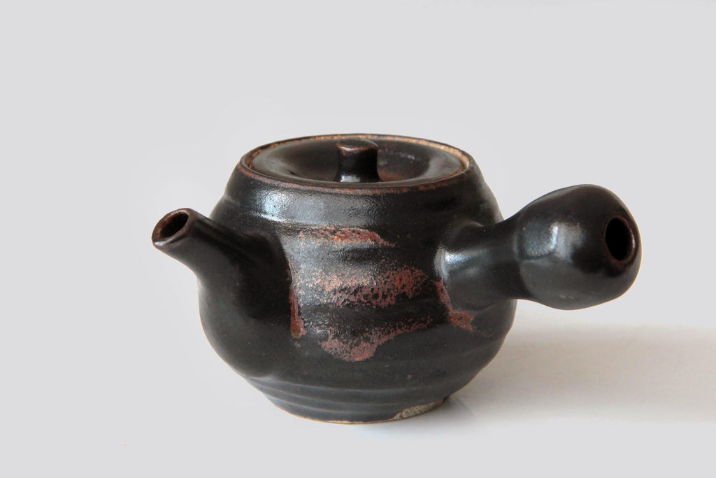 Black Satsuma ware kyusu teapot with reddish firing marks, shown from side view