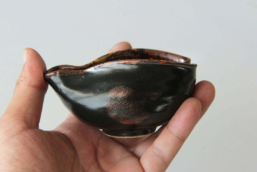 Hand holding a Japanese yuzamashi with black glaze and reddish brown patches