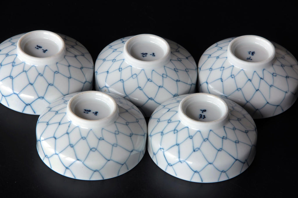 Group of five Japanese porcelain bowls upside down showing blue net pattern and base markings