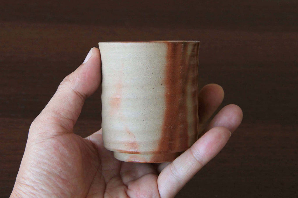 Hand holding a Bizen ware cup, showing its size and the reddish vertical firing pattern