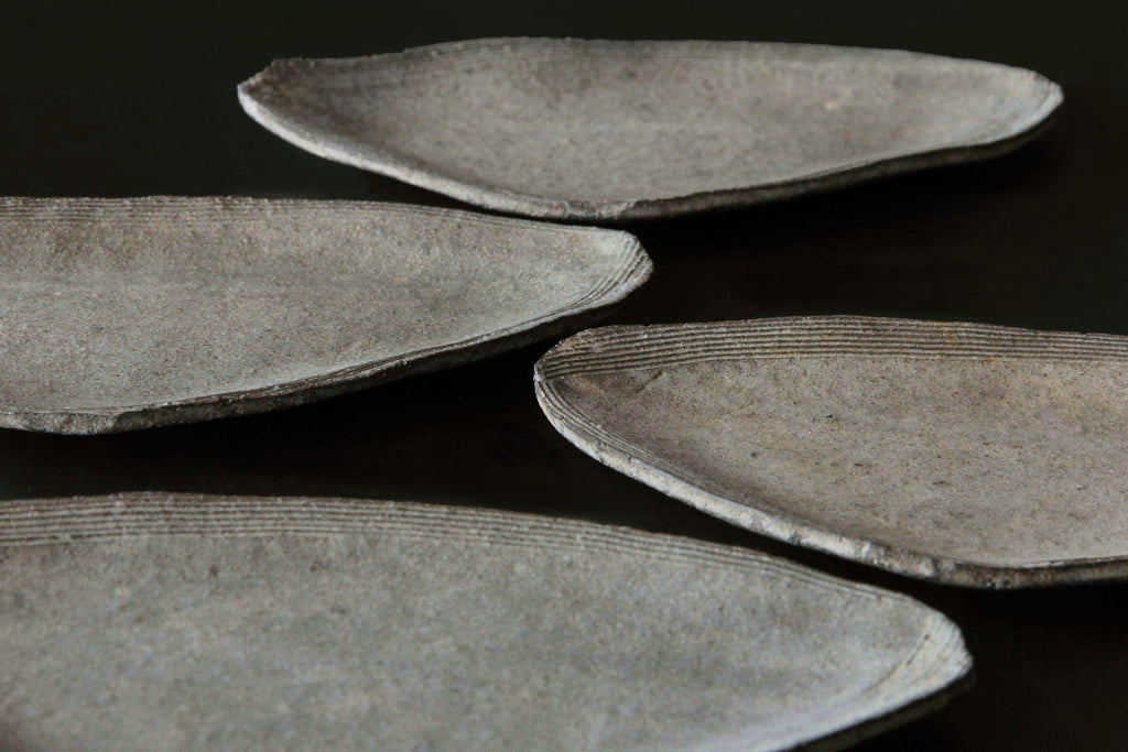 Thin rustic ceramic plate with softly curved edges and carved linear rim detail in muted earthy tone.