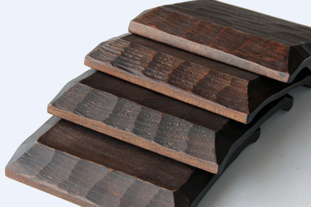 Stack of Japanese hand-carved wooden plates with dark brown finish, highlighting the textured chiseled edges.