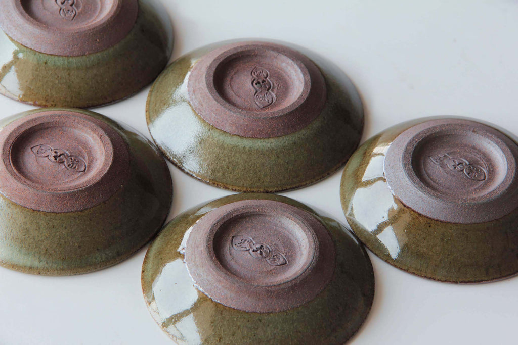 Group of Japanese small dishes shown upside down, highlighting the reddish clay foot with stamped maker’s marks.