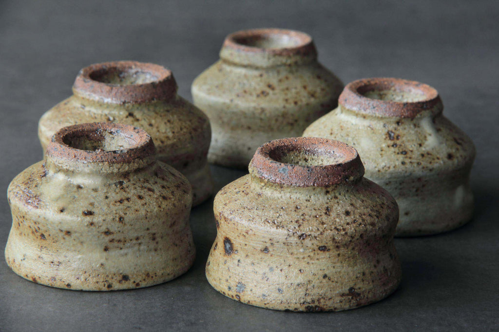 Five small ceramic cups seen from the bottom, reddish clay
foot contrasting beige glaze.