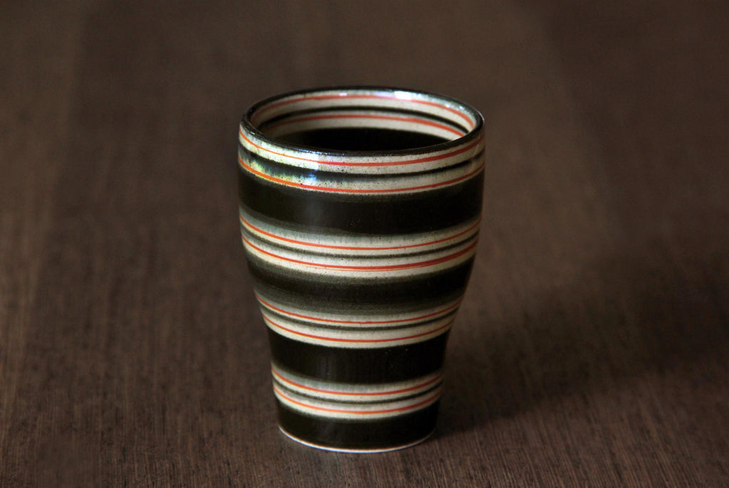 Front view of a striped Hasami ware
yunomi cup on dark wood surface,
showcasing smooth curve and glaze
lines