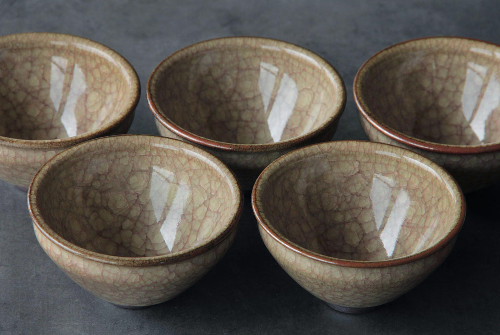 Set of five crackle glaze tea bowls arranged in semi circle on gray surface