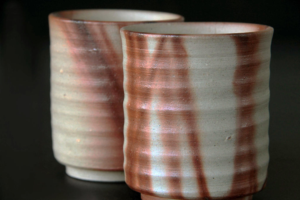 Close-up of two Bizen ware tea cups showing iridescent hidasuki markings under lighting