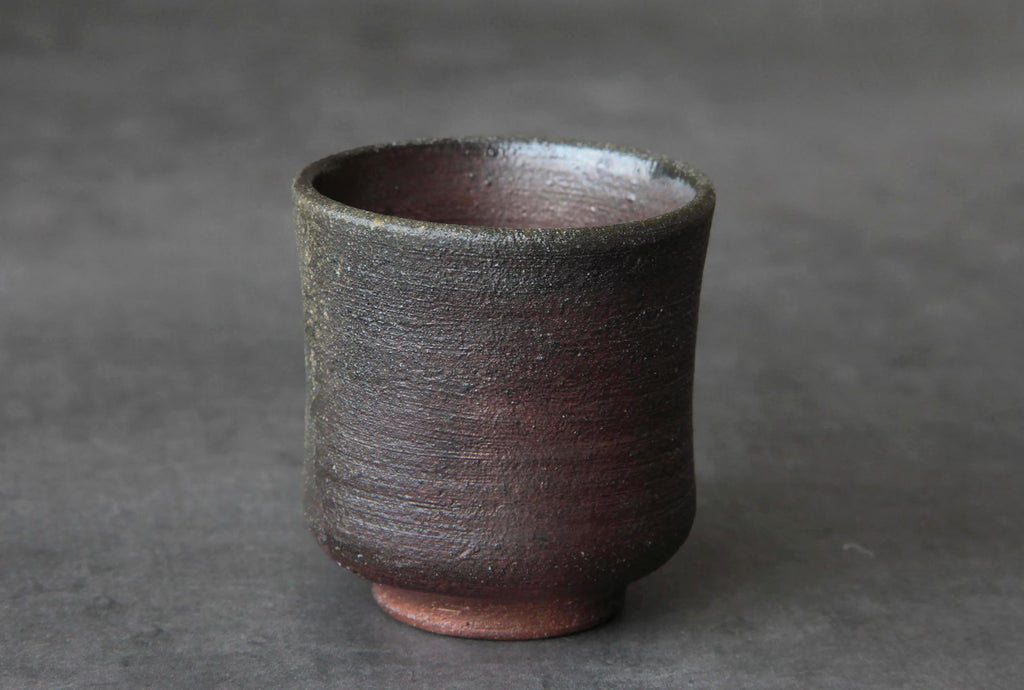 Bizen ware yunomi tea cup with natural reddish-brown clay surface and kiln-fired texture, displayed against a dark background
